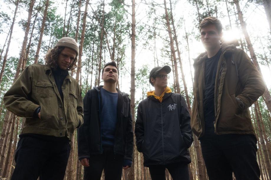 die Bandmitglieder stehen in einem Wald und werden von unten fotografiert. zweck des fotos ist die aufnahme des offiziellen bandfotos